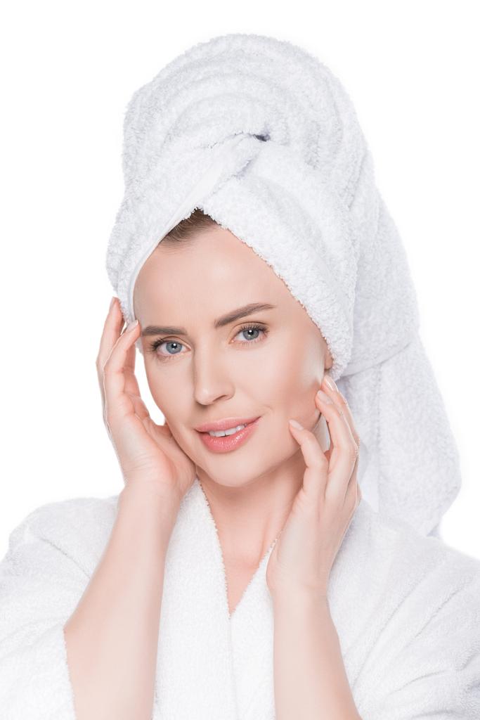Porträt einer Frau mit sauberer Haut im Bademantel und Handtuch auf dem Haar, die ihr eigenes Gesicht berührt, isoliert auf weißem Grund - Foto, Bild