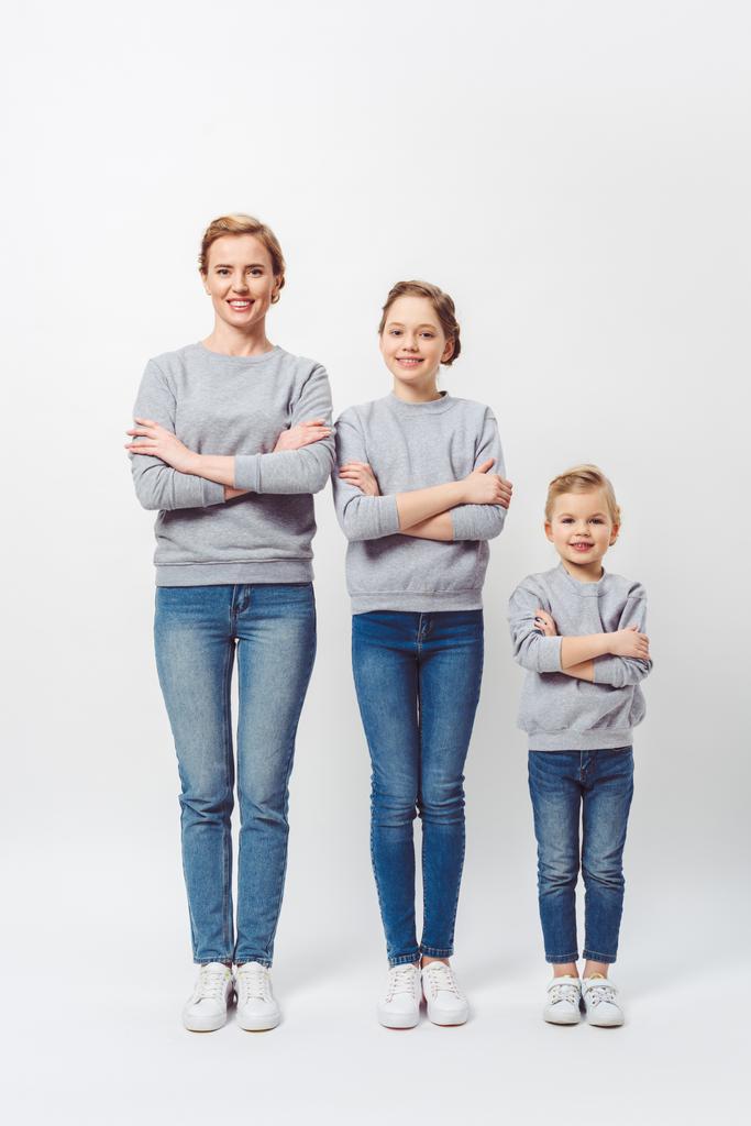 smiling mother and daughters of different generations in similar clothing with arms crossed isolated on grey - Photo, Image
