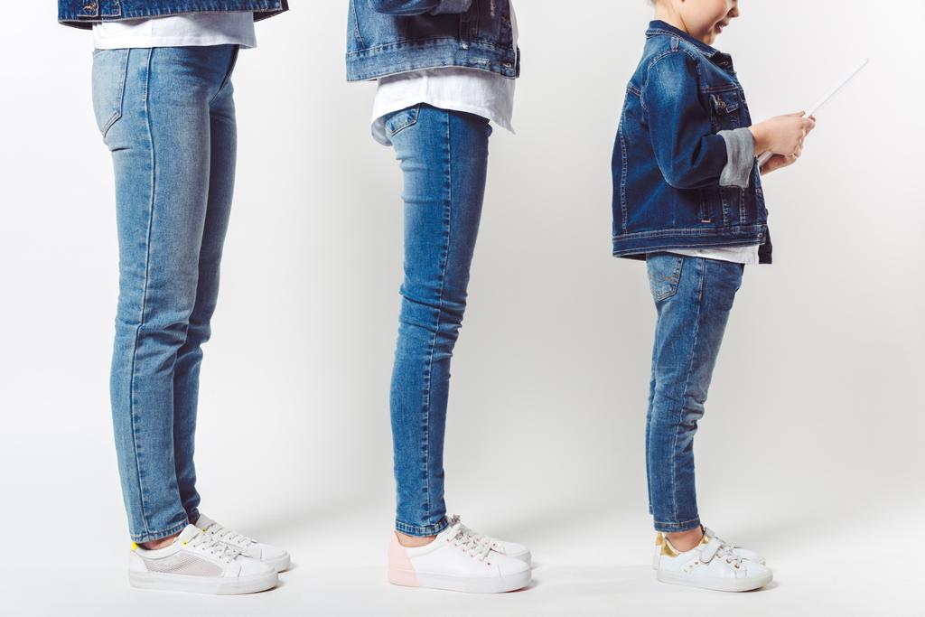 Teilansicht von Familie und Kind mit Tablet in ähnlicher Jeanskleidung, die isoliert in Reihe auf grau stehen - Foto, Bild