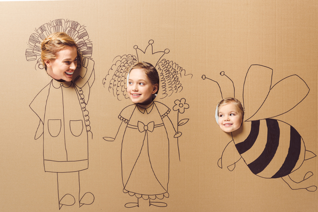 частичный вид улыбающейся матери и дочерей с головами в картонной бумаге с картинками
 - Фото, изображение