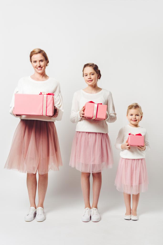 smiling mother and little daughters in similar pink tutu tulle skirts with wrapped gifts isolated on grey - Photo, Image
