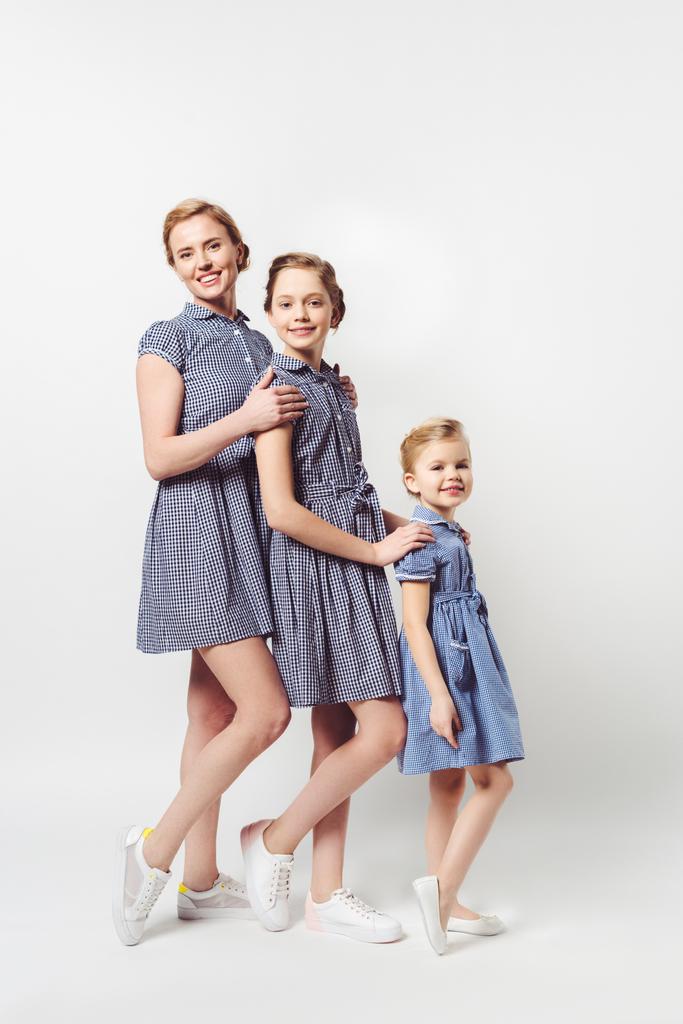мать и дочери в одинаковых платьях стоят в ряд на белом
 - Фото, изображение