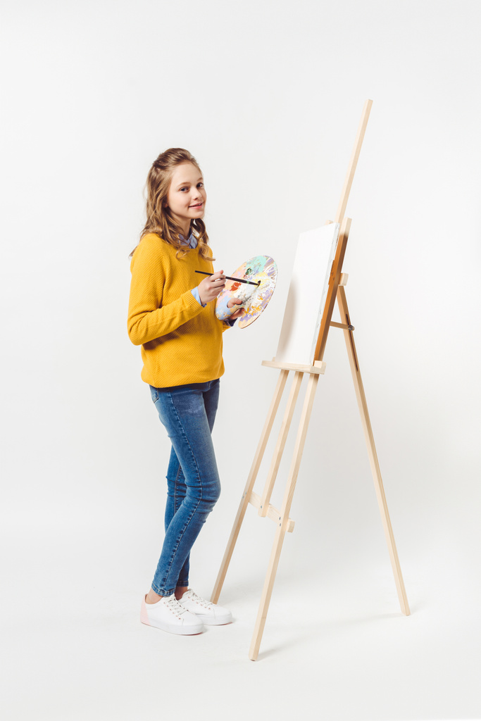 Nastolatka, Kobieta malarz z pędzlem i palety w pobliżu sztalugi z pustym płótnie na białym - Zdjęcie, obraz