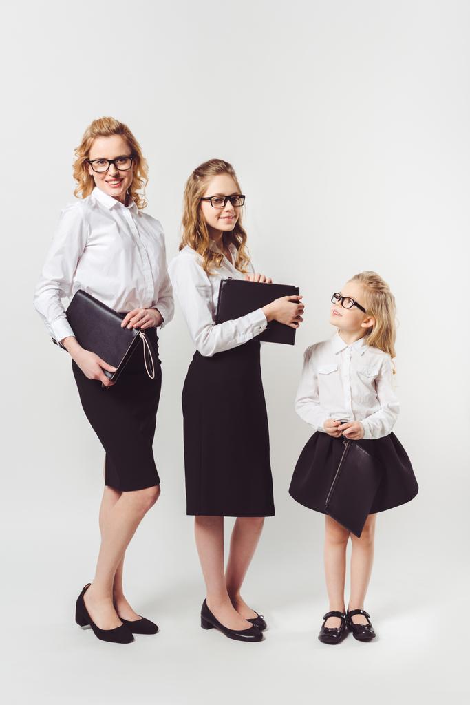 mother and daughters in similar businesswomen costumes with clutches on white - Photo, Image