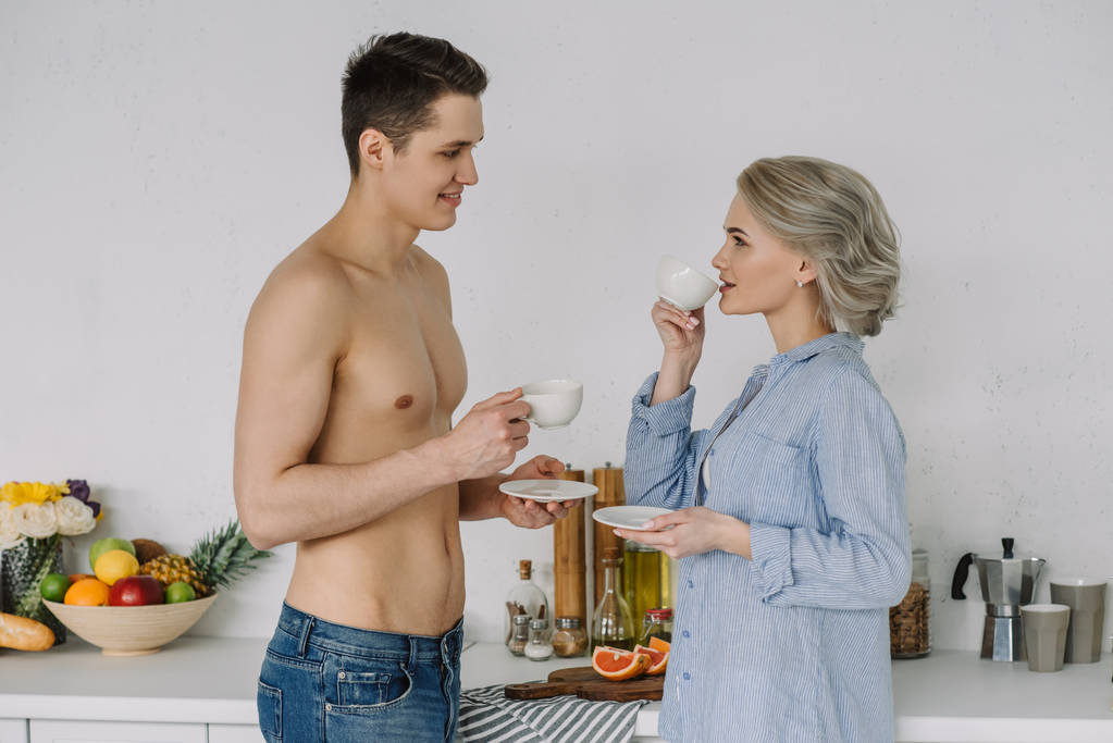 shirtless vriendje en vriendin in unbuttoned shirt drinken koffie in de ochtend - Foto, afbeelding