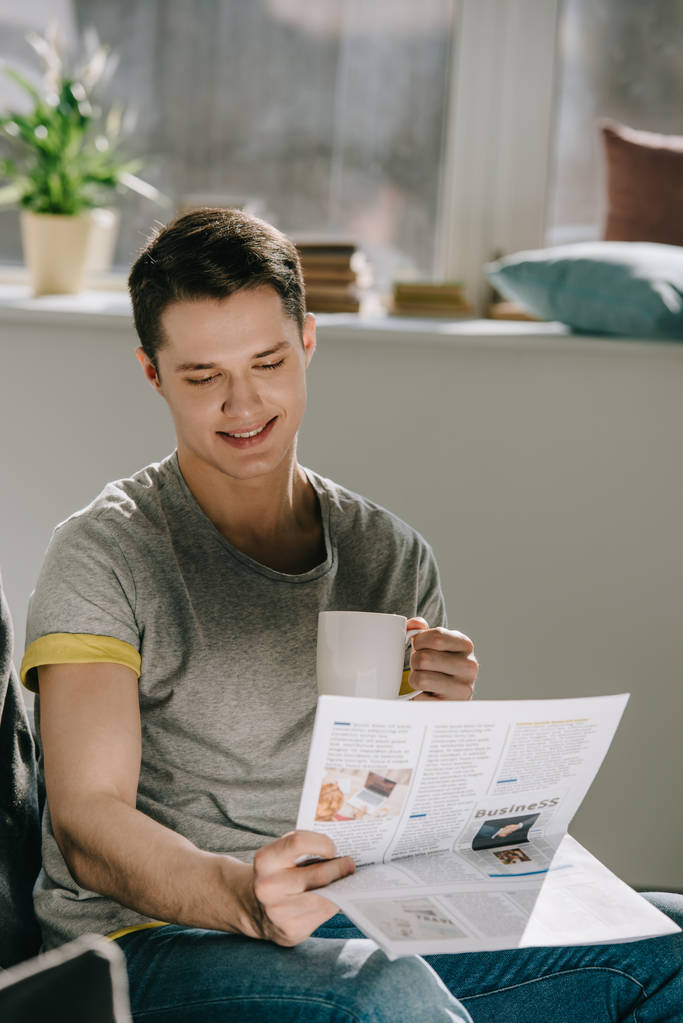 Όμορφος άντρας πίνει καφέ και διαβάζει εφημερίδα στο σπίτι. - Φωτογραφία, εικόνα