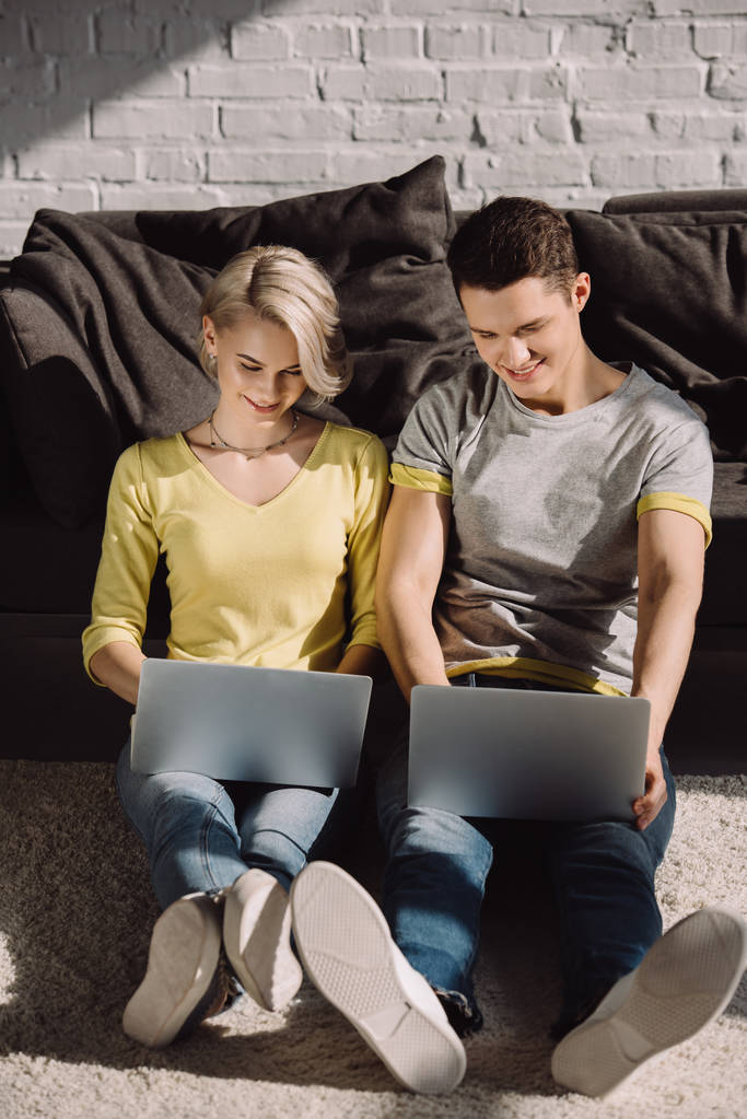 ζευγάρι κάθεται στο πάτωμα και χρησιμοποιώντας δύο φορητούς υπολογιστές στο σπίτι - Φωτογραφία, εικόνα