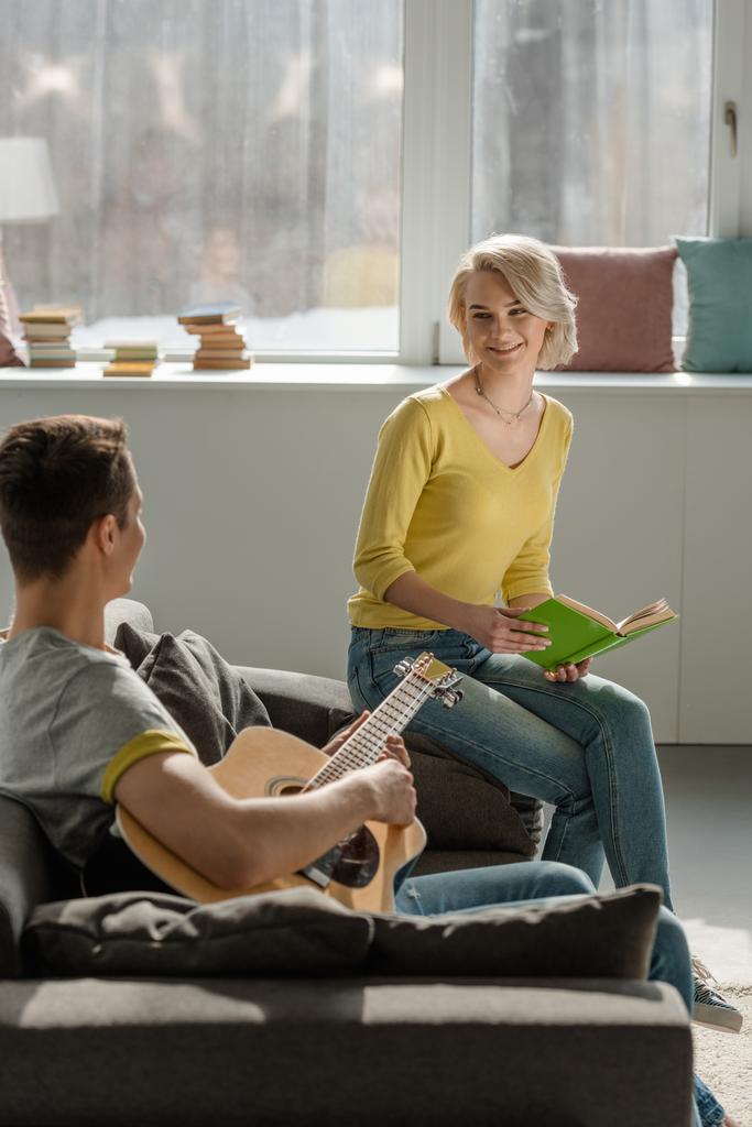 poikaystävä tilalla akustinen kitara ja tyttöystävä tilalla kirja sohvalla
 - Valokuva, kuva