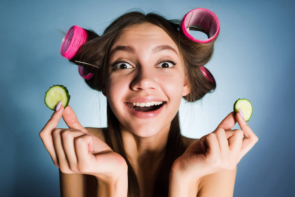 happy woman with curlers on her head holding cucumbers in her hands - Photo, Image