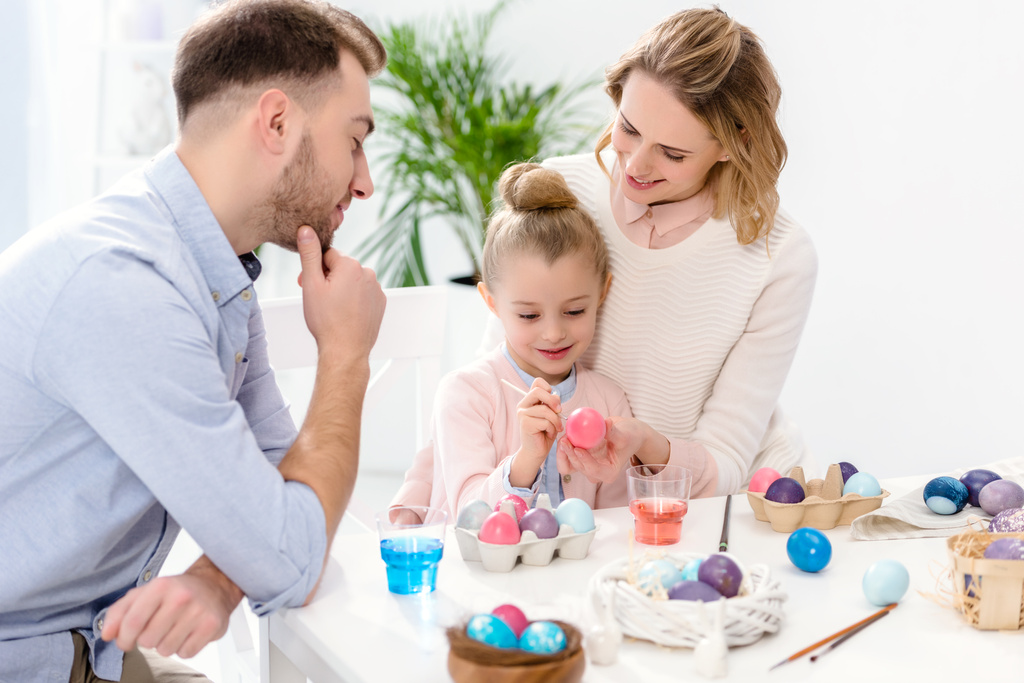 Padres e hija pintando huevos de Pascua en diferentes colores
 - Foto, Imagen