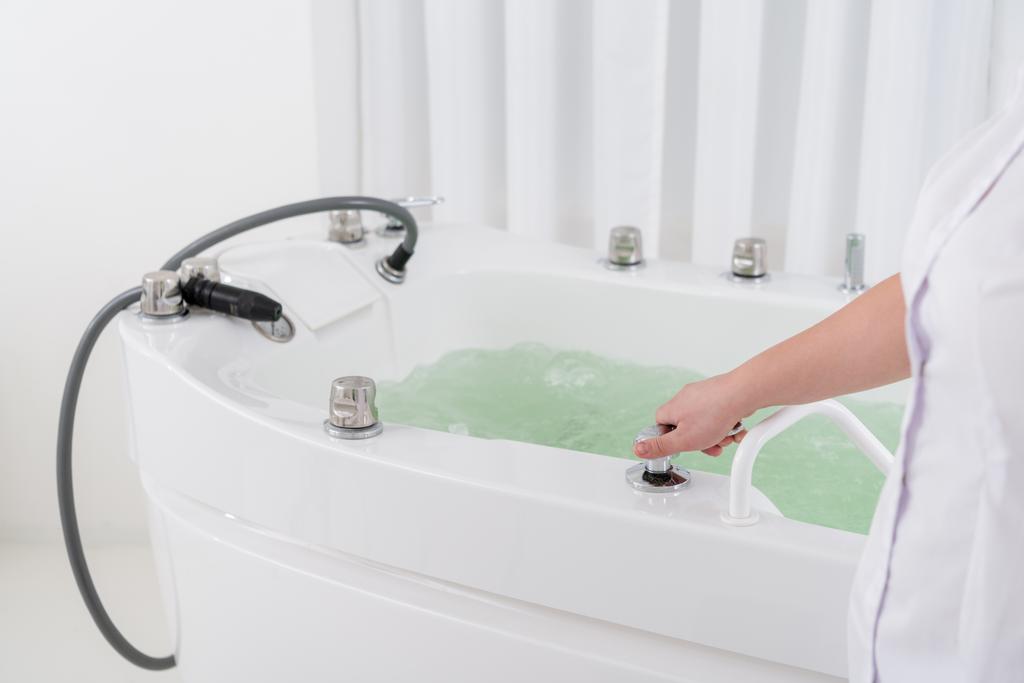 shot van de spa salon assistent regulerende water bijgesneden in hidromassage bad - Foto, afbeelding