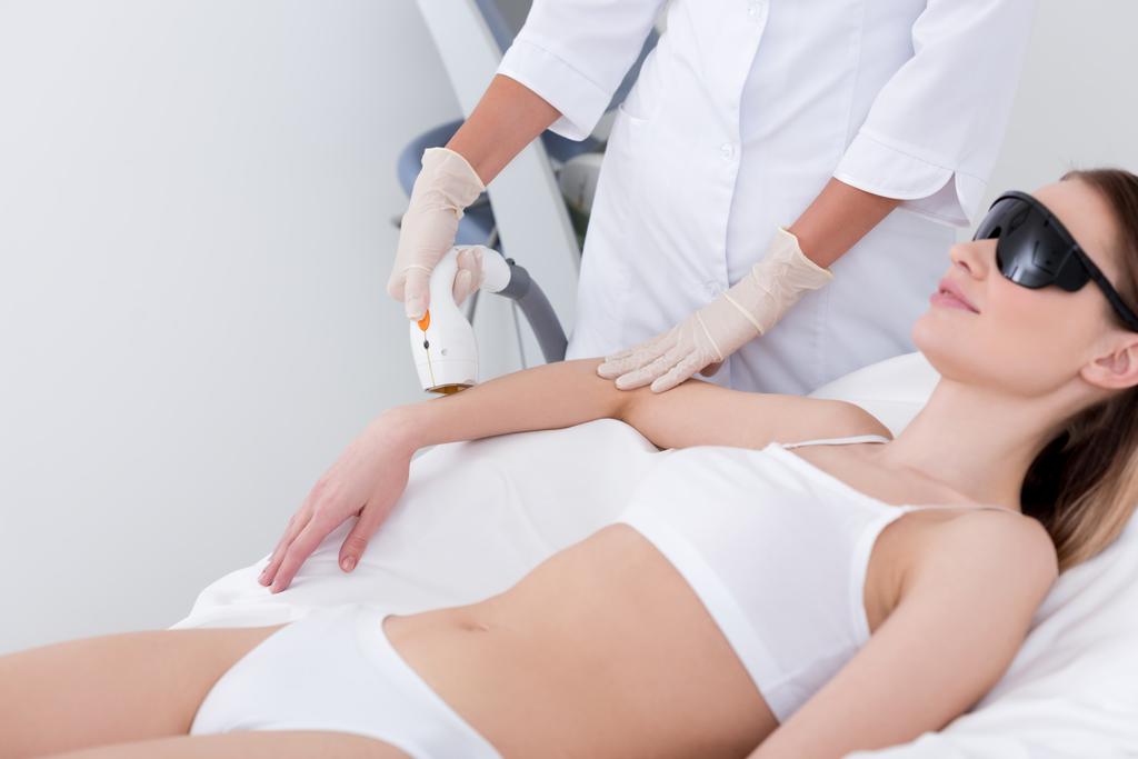 bijgesneden schot van vrouw krijgen van laser hair removal procedure op arm in salon - Foto, afbeelding