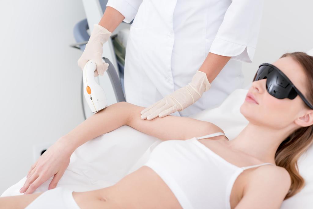 partial view of woman receiving laser hair removal procedure on arm made by cosmetologist in salon - Photo, Image