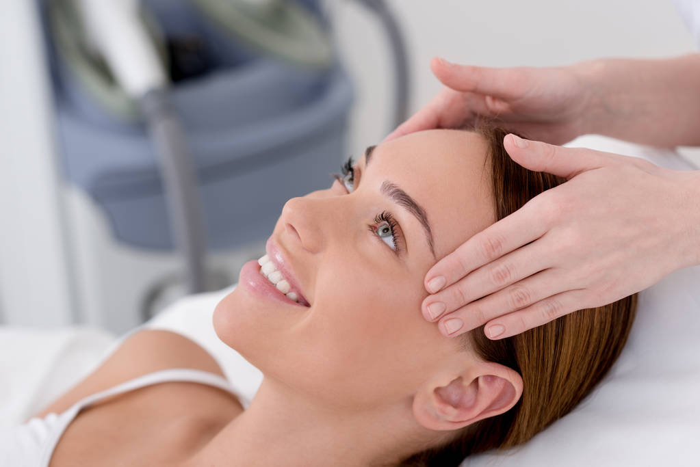 частковий вид на молоду жінку, що отримує масаж голови, зроблений косметологом у салоні
 - Фото, зображення