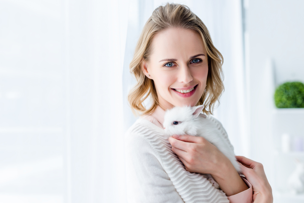 Blonde vrouw knuffelen wit konijntje door raam - Foto, afbeelding