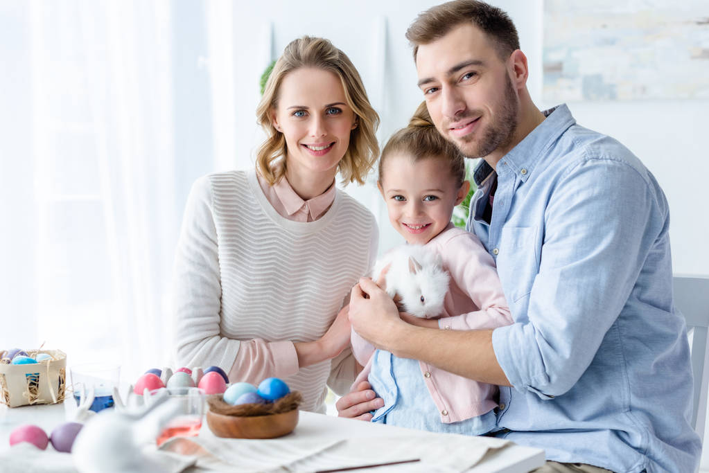 glückliche Familie hält Osterhasen mit Ostereiern auf dem Tisch - Foto, Bild