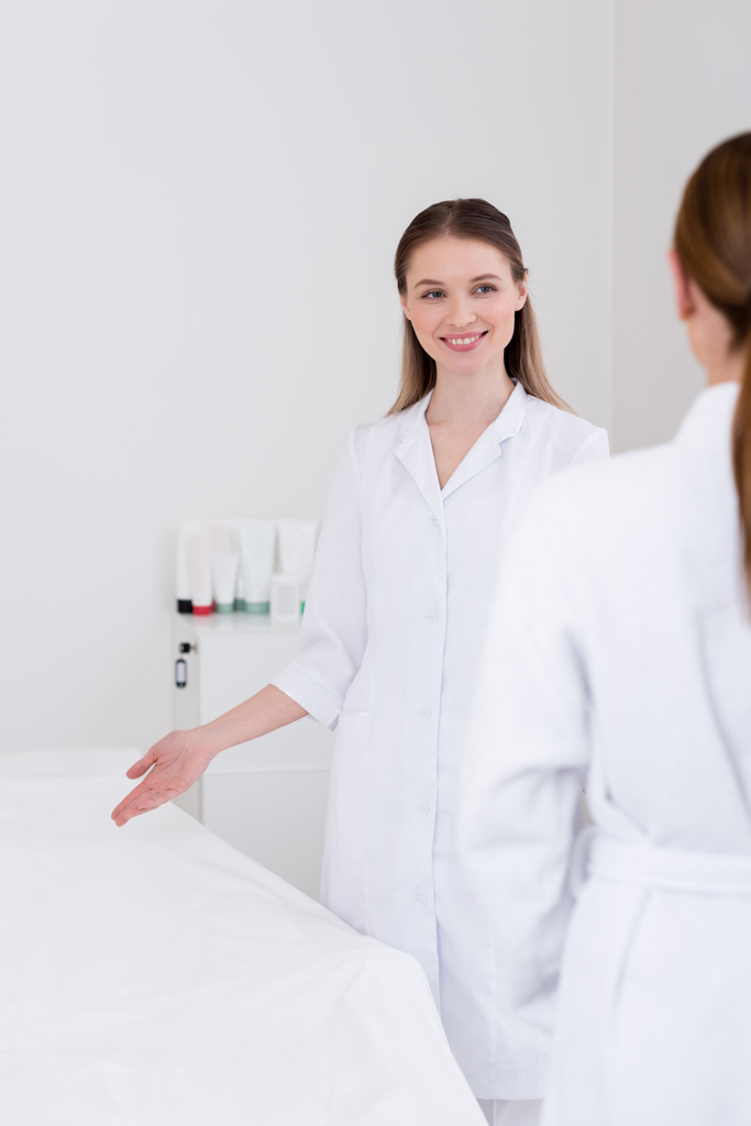 cosmetologista sorridente em casaco branco e cliente no salão
 - Foto, Imagem