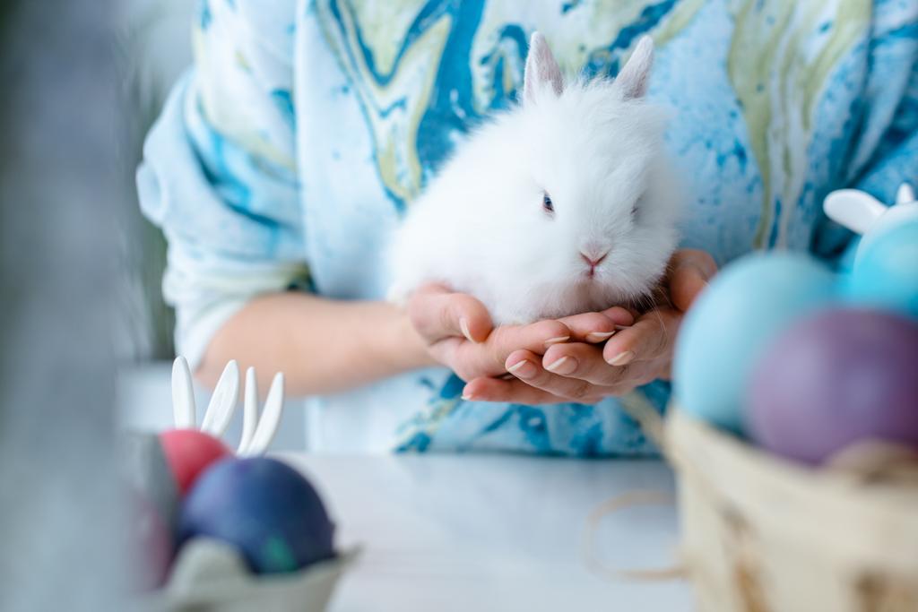 Жінка тримає кролика кольоровими великодніми яйцями на столі
 - Фото, зображення