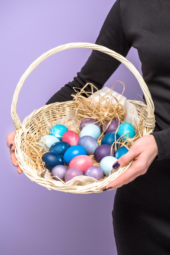Mujer sosteniendo huevos de Pascua en cesta aislada en violeta
 - Foto, imagen