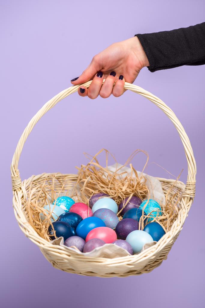 Mão feminina com cesta de Páscoa com ovos coloridos isolados em violeta
 - Foto, Imagem