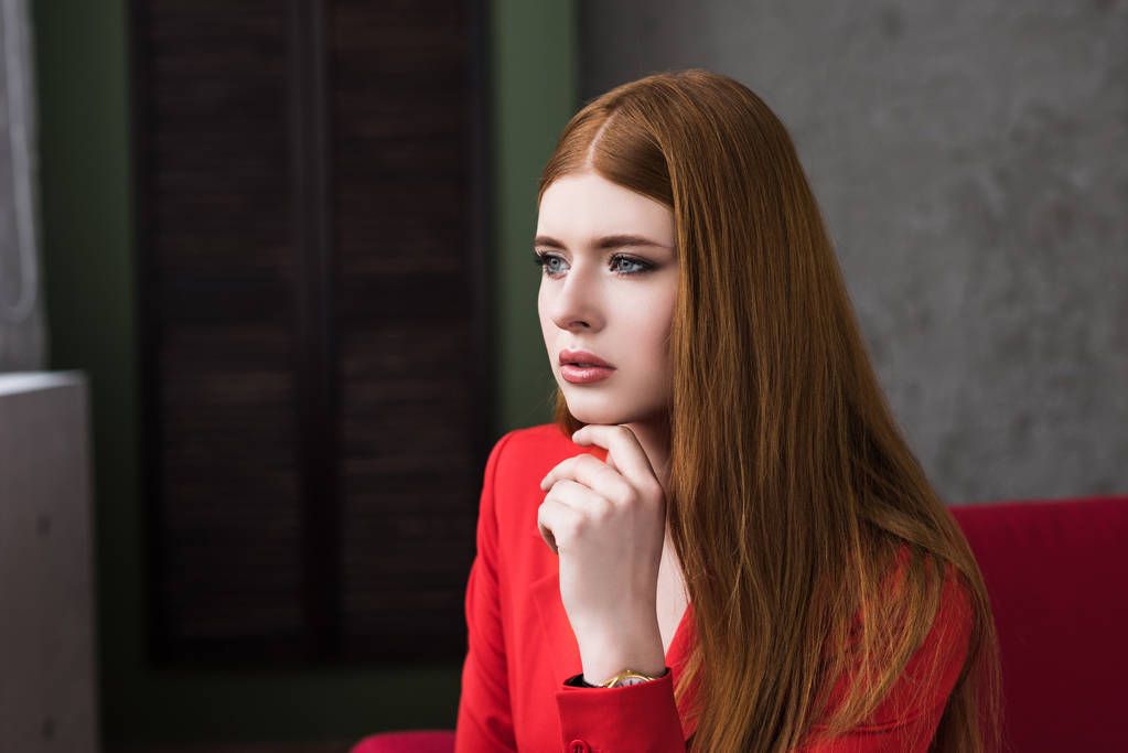 Jonge vrouwelijke model gekleed in rood jasje houden vinger op kin - Foto, afbeelding