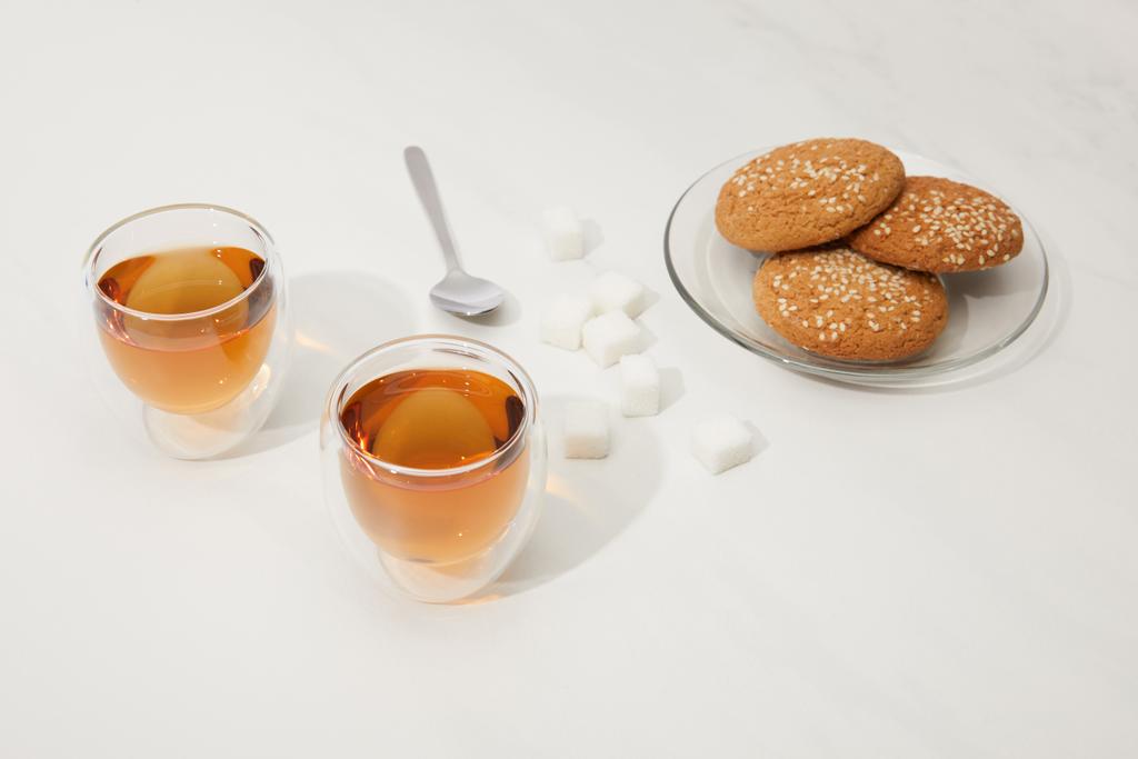 close-up view of tea in glass cups, spoon, sugar cubes and oatmeal cookies on plate on grey  - Photo, Image
