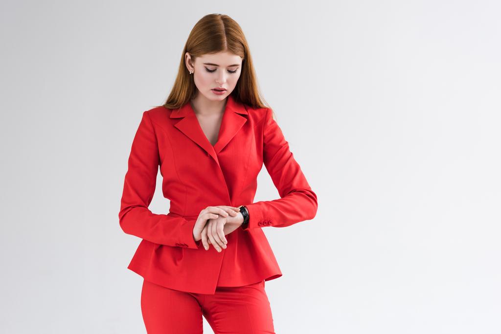 junge stilvolle Frau im Anzug schaut auf Armbanduhr isoliert auf grau - Foto, Bild