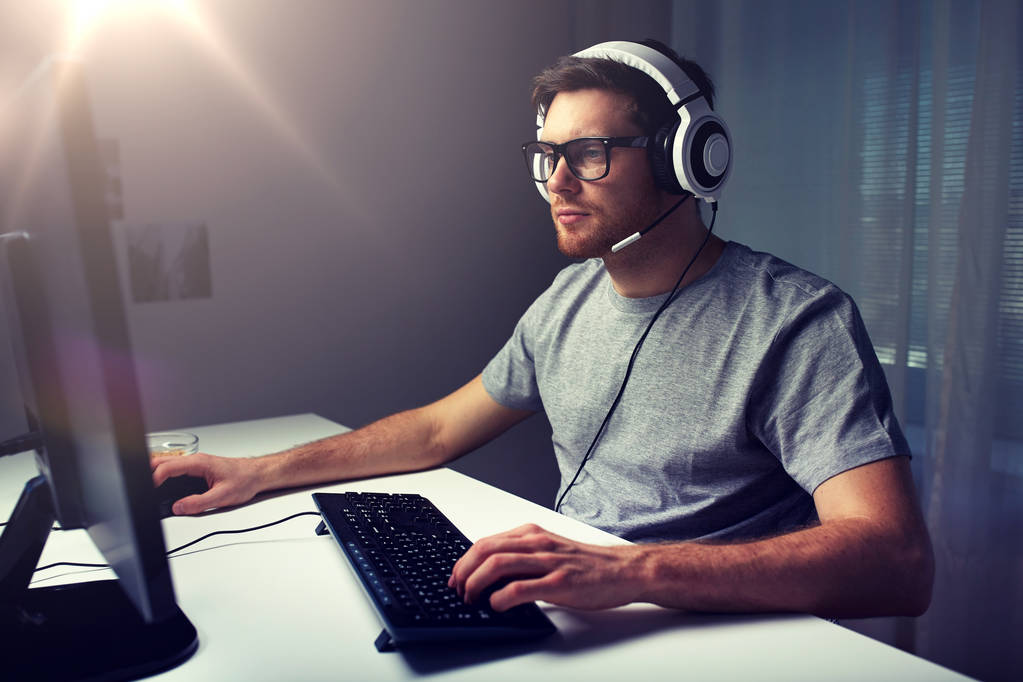 mies kuulokkeissa pelaa tietokonepeliä kotona
 - Valokuva, kuva