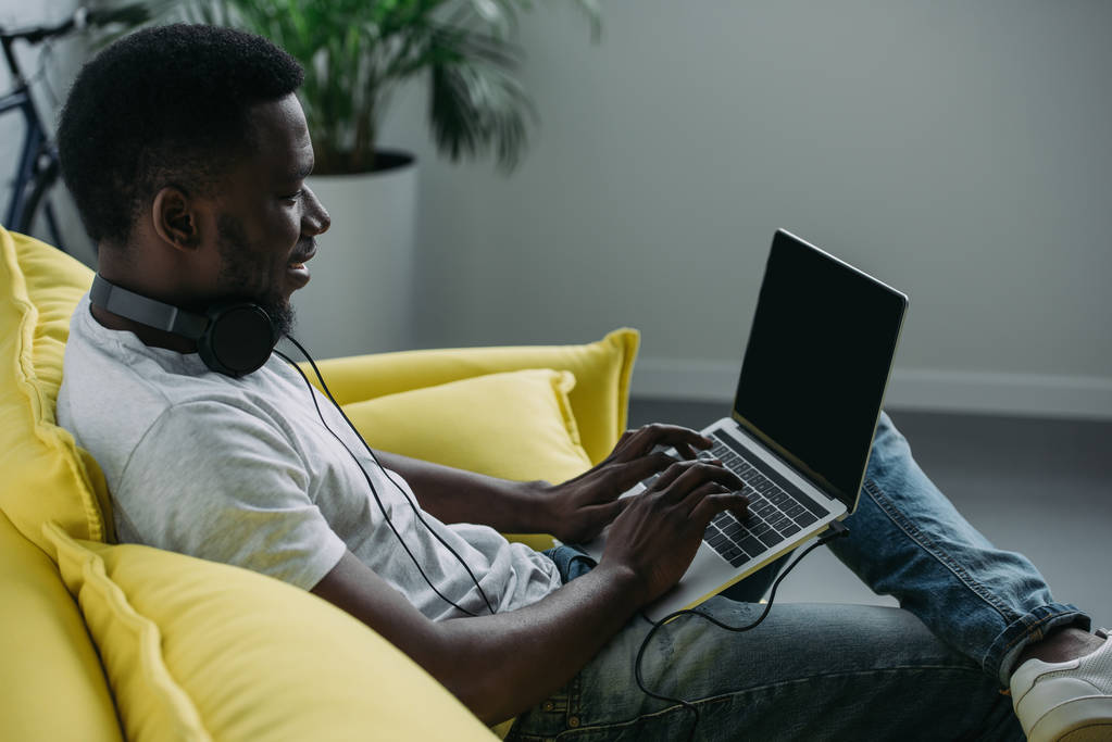 sonriente joven afroamericano hombre usando portátil con pantalla en blanco en casa
 - Foto, Imagen