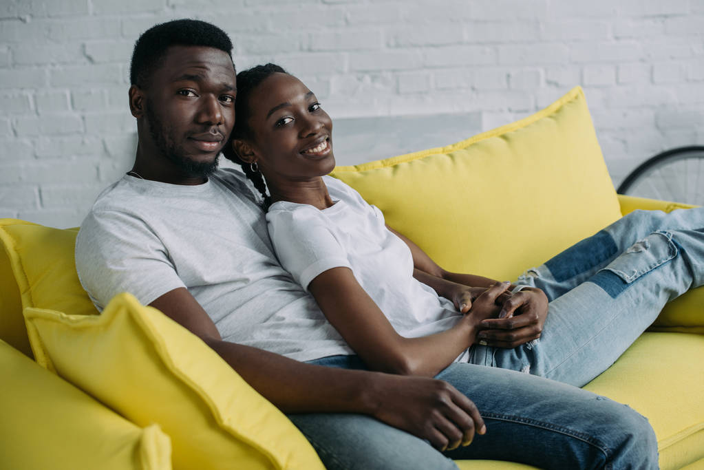 feliz joven africano americano pareja sentado en sofá y sonriendo a la cámara
 - Foto, imagen