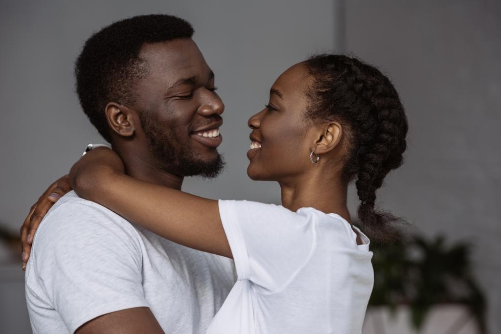 gelukkige jonge Afro-Amerikaanse paar knuffelen en glimlachen elkaar thuis - Foto, afbeelding