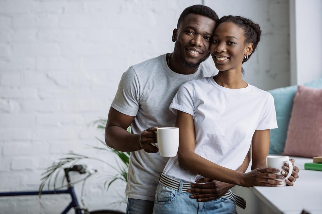 felice giovane coppia afro-americana che tiene le tazze e sorride alla macchina fotografica
 - Foto, immagini