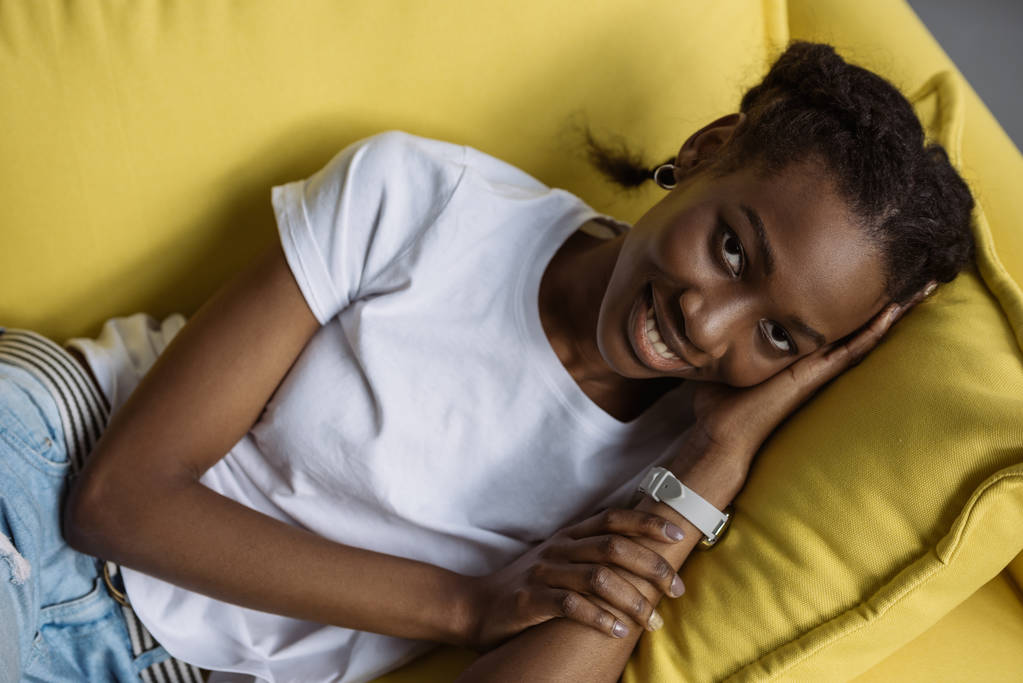 gyönyörű fiatal afrikai-amerikai nő feküdt a kanapén, és mosolyogva kamera - Fotó, kép