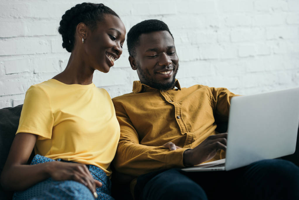 χαρούμενος νεαρός αφρικανική αμερικανική ζευγάρι χρησιμοποιώντας φορητό υπολογιστή μαζί στο σπίτι - Φωτογραφία, εικόνα