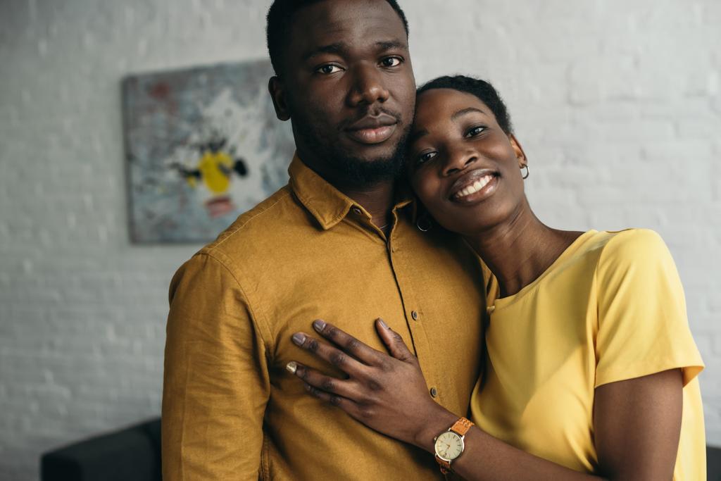 νεαρός αφρικανική αμερικανική ζευγάρι σε κίτρινο πουκάμισα, στέκεται μαζί και βλέπουν κάμερα στο σπίτι - Φωτογραφία, εικόνα