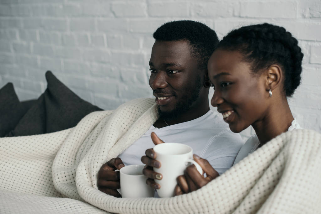 onnellinen nuori afrikkalainen amerikkalainen pari, jolla on kuppeja teetä ja katselee pois kotiin
  - Valokuva, kuva