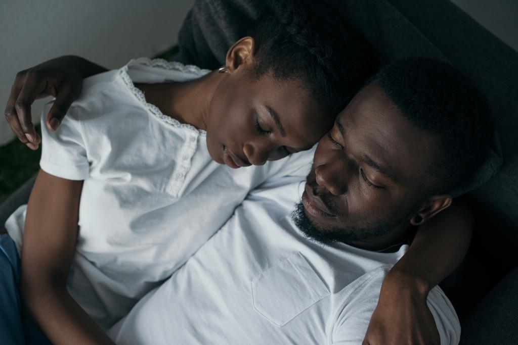 schönes junges afrikanisch-amerikanisches Paar umarmt, während es zu Hause auf dem Sofa schläft - Foto, Bild