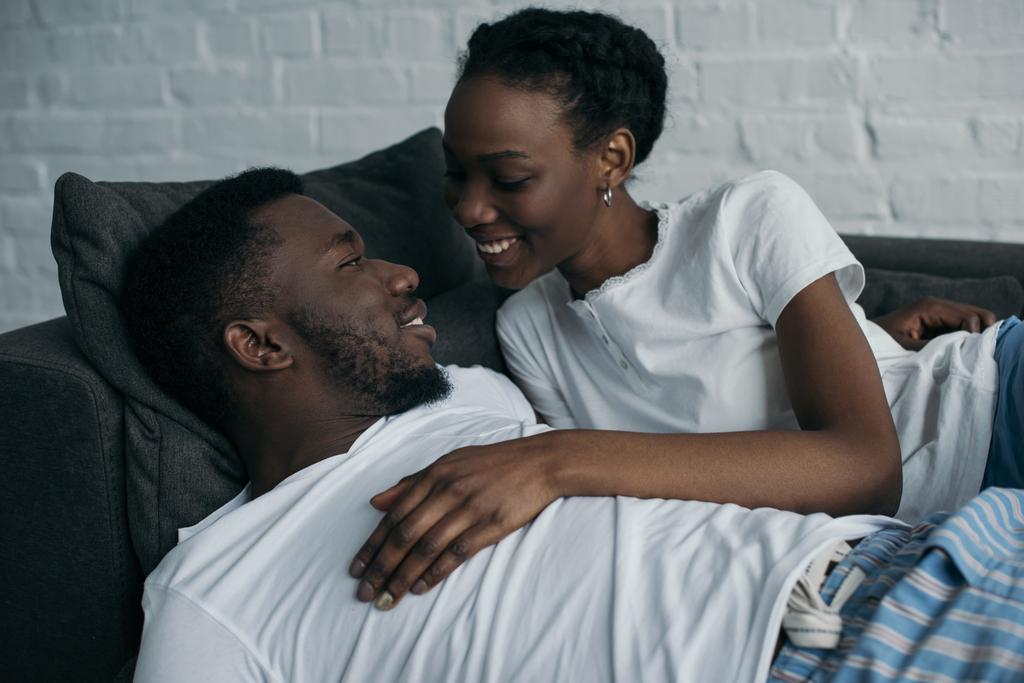 家庭でお互いに笑みを浮かべてのパジャマを着て美しい幸せな若いアフリカ系アメリカ人カップル   - 写真・画像
