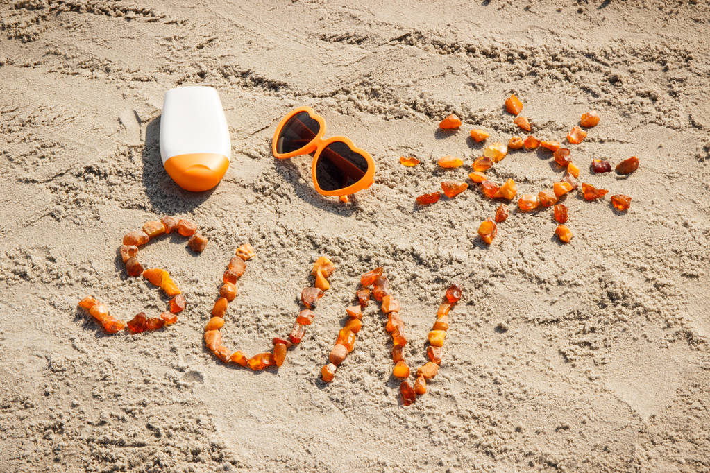 Λέξη και το σχήμα του ήλιου, γυαλιά ηλίου με ήλιο λοσιόν στην άμμο στην παραλία, θερινή ώρα έννοια - Φωτογραφία, εικόνα