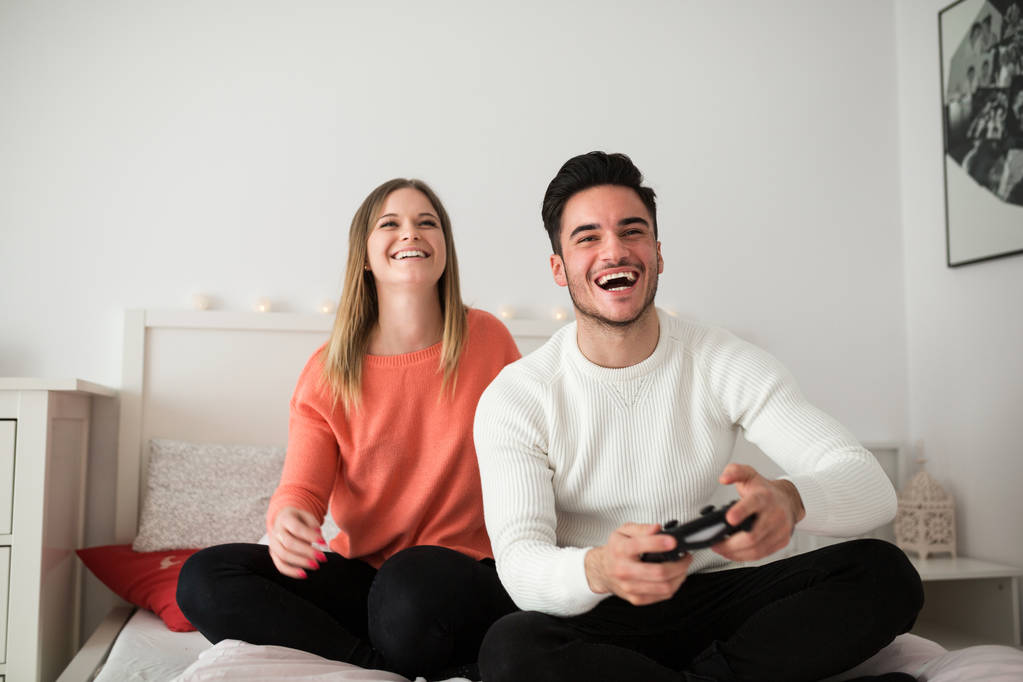 Νεαρό ζευγάρι παίζοντας βιντεοπαιχνίδια στο κρεβάτι - Φωτογραφία, εικόνα