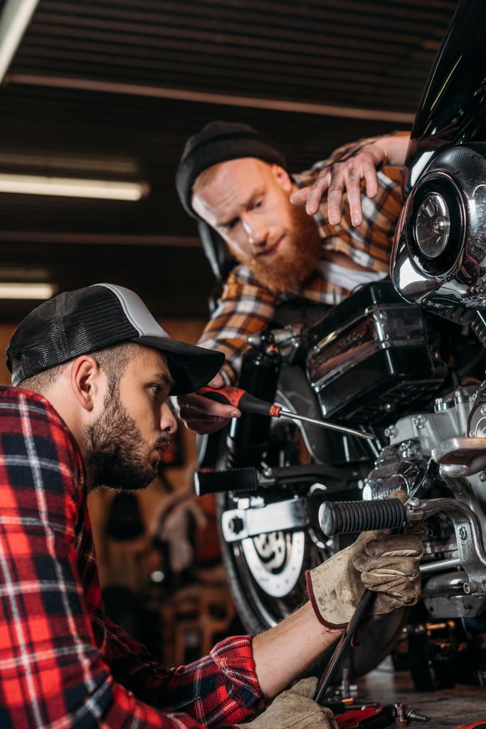 pohledný mladý mechanika společně opravy motocyklů v garáži - Fotografie, Obrázek