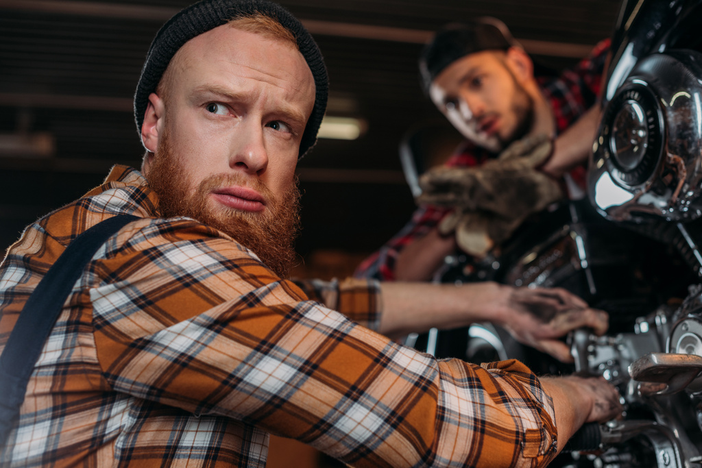 gutaussehende Mechaniker schauen weg, während sie Motorräder in der Garage reparieren - Foto, Bild