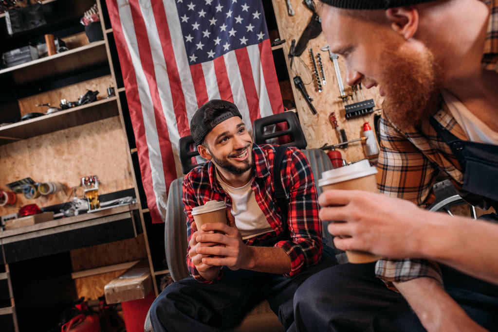 mecánicos guapos beber café de tazas desechables en el descanso en el garaje
 - Foto, imagen