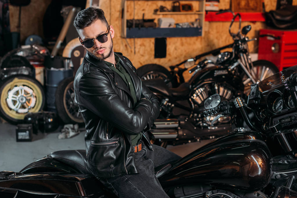 красивый молодой человек в солнцезащитных очках и кожаной куртке на велосипеде в гараже
 - Фото, изображение