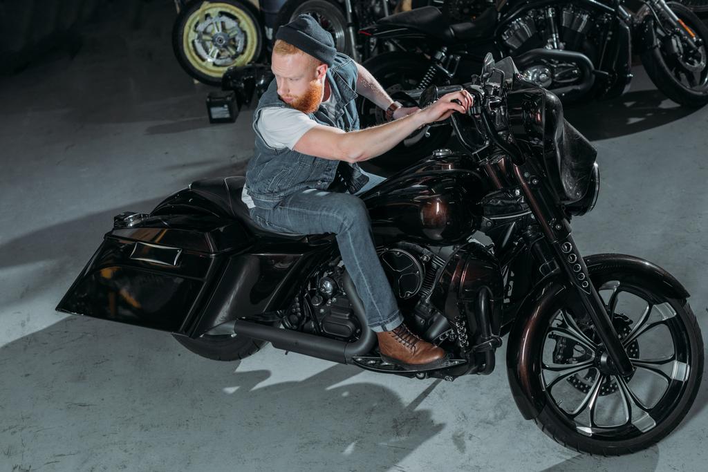 vysoký úhel pohled pohledný mladý muž na motocyklu v garáži - Fotografie, Obrázek