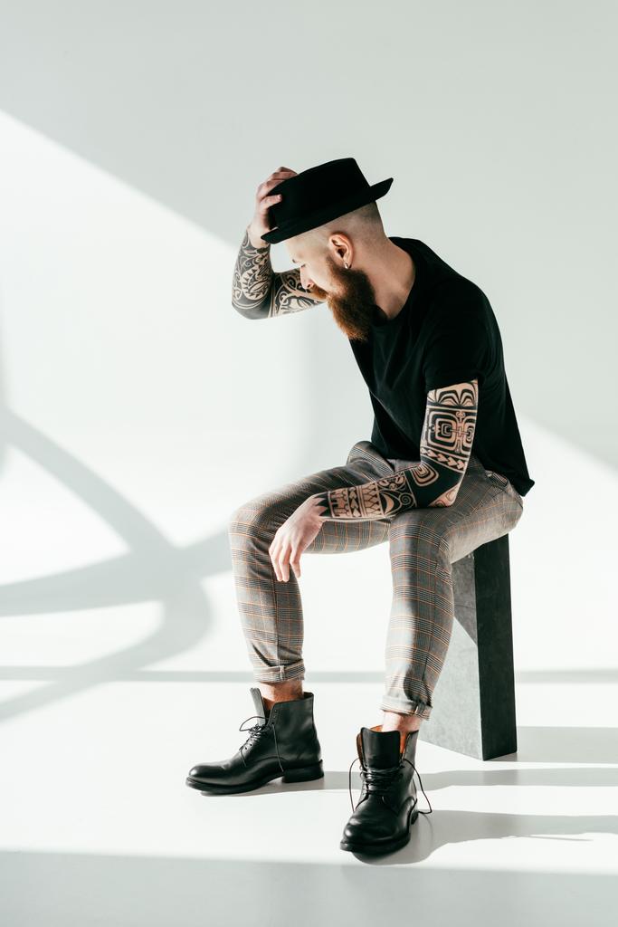 όμορφος γενειοφόρος άνδρας τατουάζ αγγίζοντας καπέλο λευκό - Φωτογραφία, εικόνα