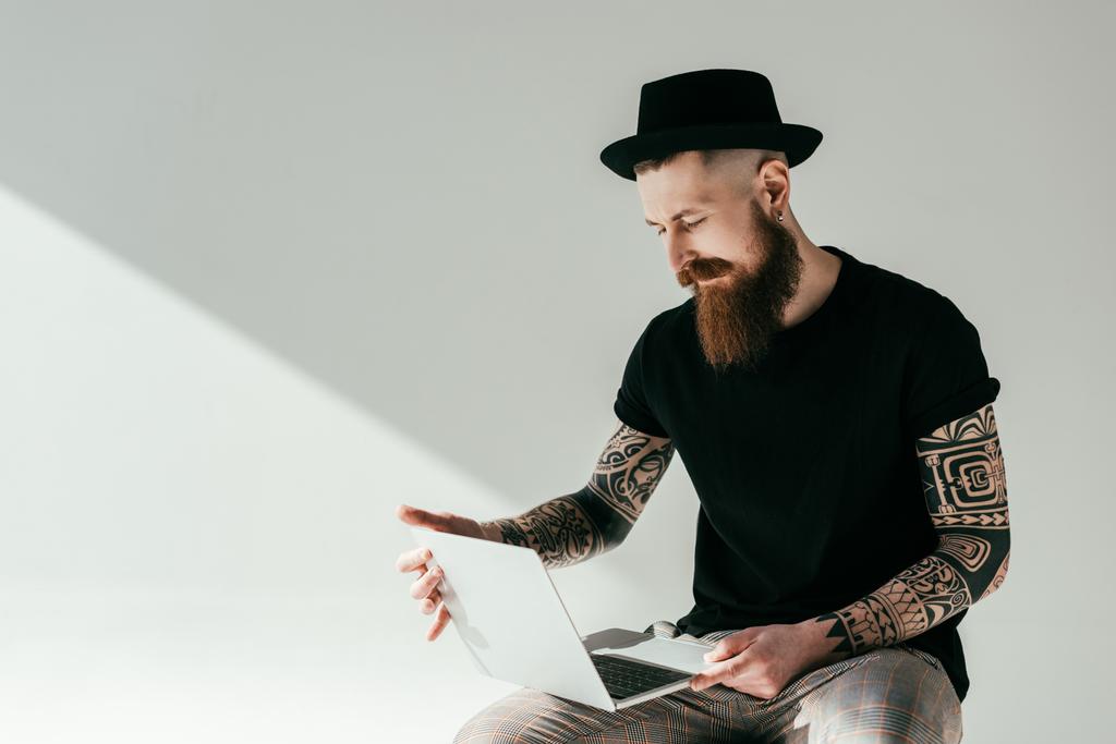 όμορφος γενειοφόρος άνδρας τατουάζ που εργάζονται με το laptop σε λευκό - Φωτογραφία, εικόνα