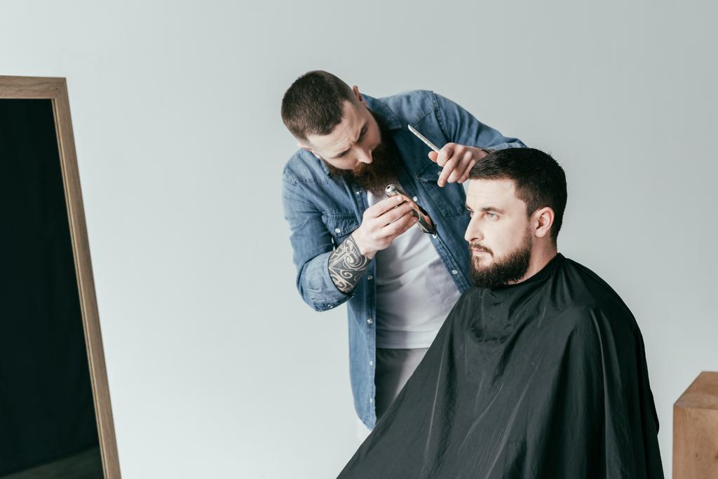 Friseur schneidet gutaussehenden Kundenbart beim Friseur isoliert auf Weiß - Foto, Bild