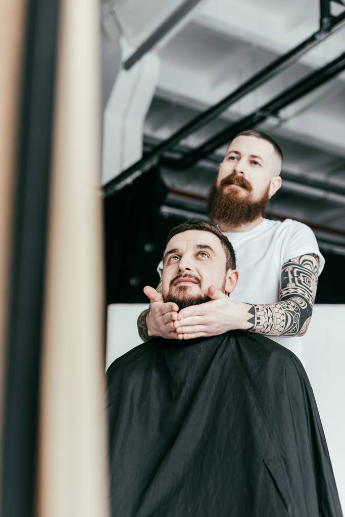 barber styling customer beard and looking at mirror at barbershop - Photo, Image