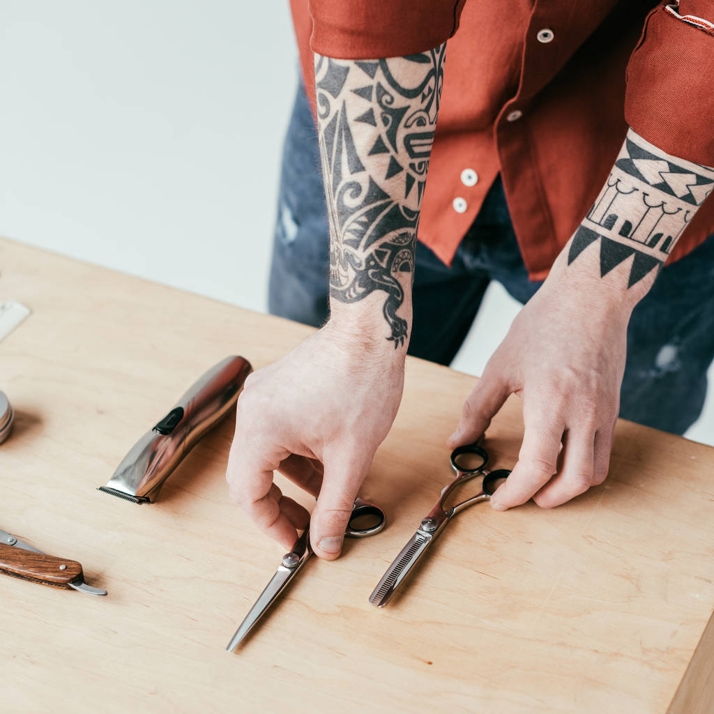 обрізане зображення татуйованого перукаря, що бере ножиці зі столу ізольовані на білому
 - Фото, зображення